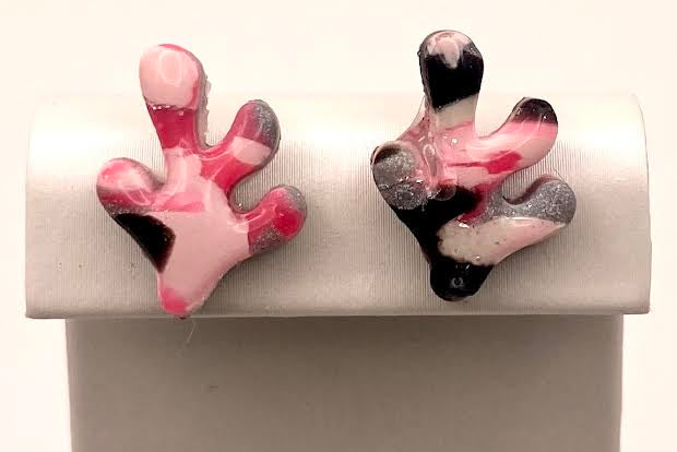 A pair of coral-shaped stud earrings with pink, black, and white marbled patterns, displayed on a white jewelry stand against a light background.