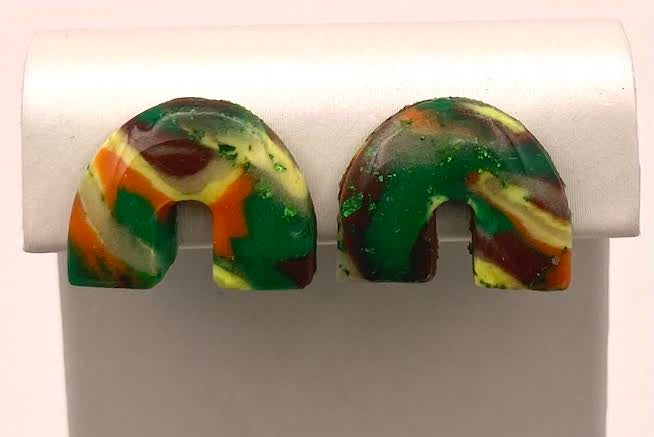 A pair of handmade resin earrings with a marbled pattern of green, orange, yellow, and dark brown, displayed on a white plastic stand.
