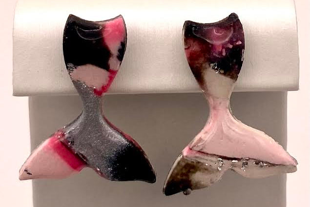 A pair of handmade mermaid tail earrings with a marbled pattern of pink, black, gray, and white, displayed on a white jewelry stand.