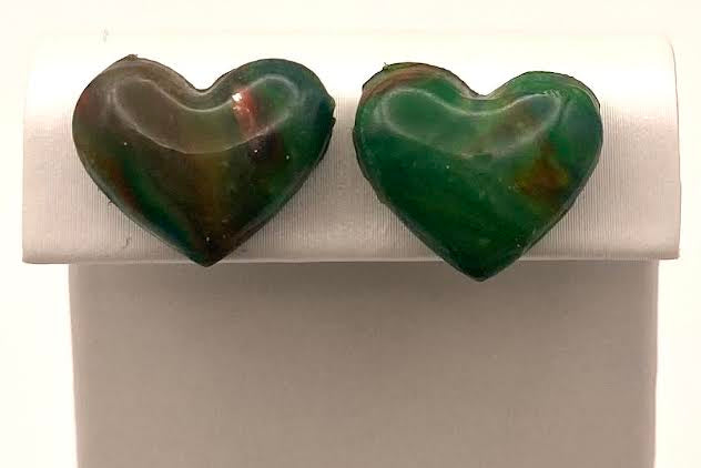 A pair of heart-shaped green gemstone stud earrings displayed on a white jewelry stand against a white background.