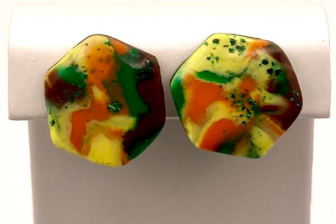 A pair of hexagonal stud earrings with a marbled, organic pattern of yellow, orange, green, and dark red, displayed on a white jewelry stand.