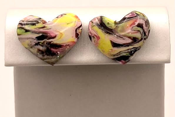 A pair of heart-shaped stud earrings with a marbled pattern of yellow, pink, black, and white, displayed on a white jewelry stand against a white background.
