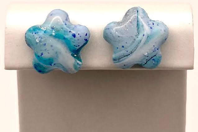 A pair of star-shaped stud earrings with a marbled blue, white, and light blue design, displayed on a white jewelry stand.