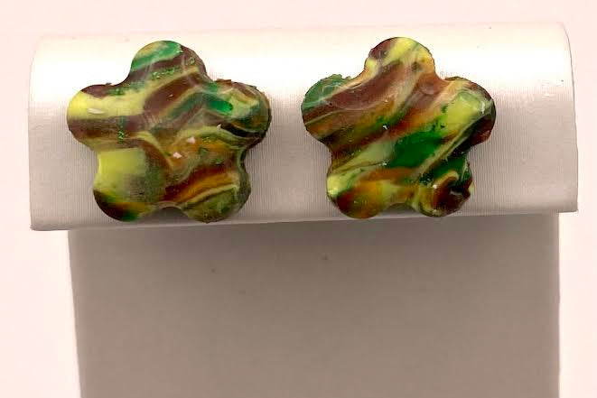 A pair of marbled green, yellow, and brown flower-shaped stud earrings displayed on a white jewelry stand against a light background.