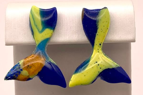 A pair of handmade glass fish tail earrings with blue, yellow, and orange marbled colors, displayed on a white jewelry stand.