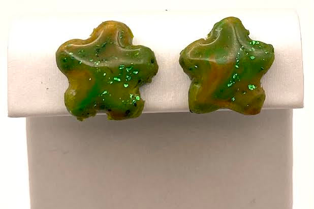 A pair of green and yellow marbled star-shaped stud earrings with glitter, displayed on a white jewelry stand against a white background.
