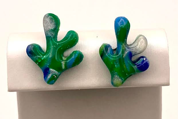 A pair of handmade glass coral stud earrings in green, blue, and white, displayed on a white jewelry stand against a white background.
