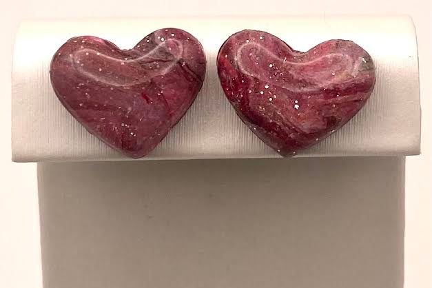 A pair of heart-shaped stud earrings with a marbled pink and white pattern, displayed on a white jewelry stand.