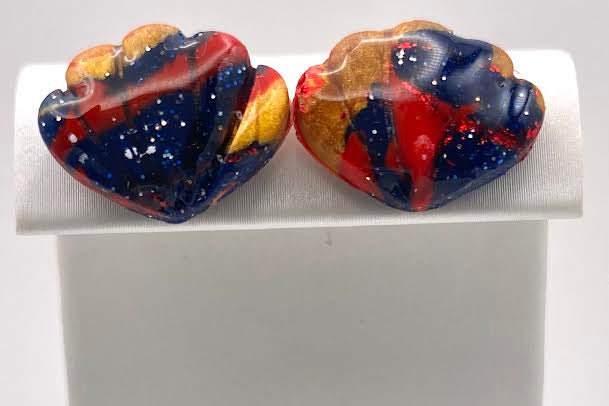 A pair of handmade heart-shaped glass stud earrings with a marbled pattern of red, blue, yellow, and white, displayed on a white jewelry stand.