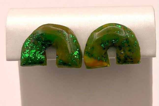 A pair of green glittery U-shaped stud earrings displayed on a white jewelry stand against a light background.