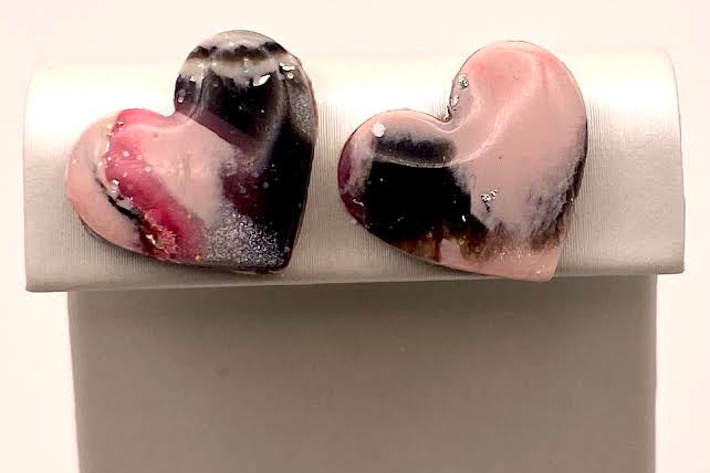 Two heart-shaped glass art pieces with a marbled swirl of pink, black, and white, displayed on a white jewelry stand.