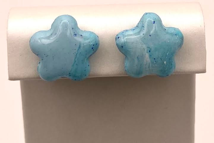A pair of light blue star-shaped stud earrings displayed on a white jewelry stand against a plain light background.