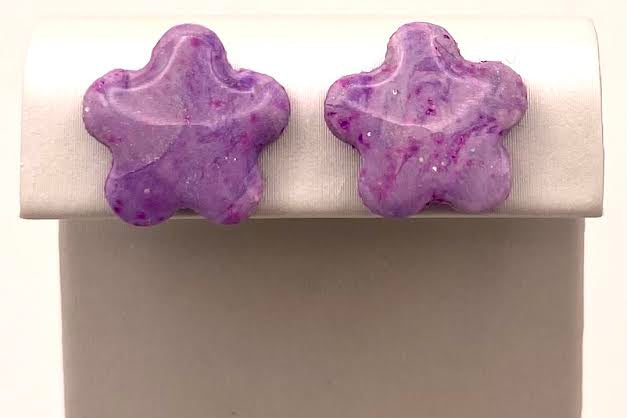 A pair of purple star-shaped stud earrings displayed on a white jewelry stand against a light background.