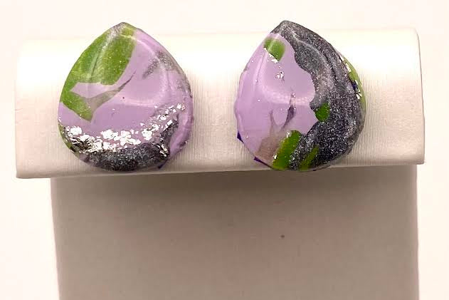 A pair of teardrop-shaped stud earrings with a marbled pattern of lavender purple, black, and green, displayed on a white jewelry stand against a white background.