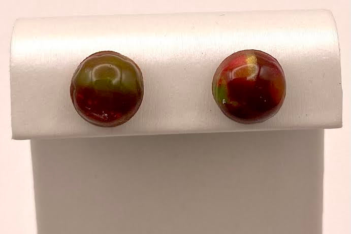 A pair of round, glossy marbled stud earrings in reddish-brown and olive green, displayed on a white jewelry stand against a light background.