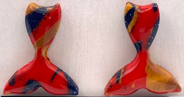 A pair of abstract sculptural earrings in a glossy red, orange, yellow, and navy blue marbled pattern, displayed on a black stand in front of a white textured card with the brand name 'Phoenix Frost Art'.