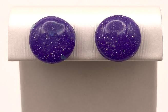 A pair of round stud earrings with a deep purple glitter finish, displayed on a white jewelry stand against a white background.