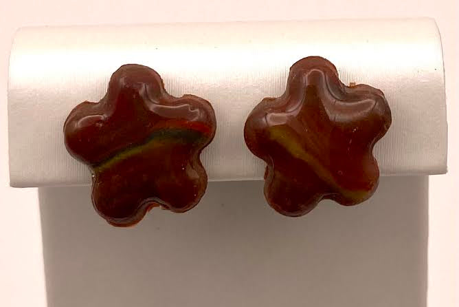 A pair of brown marbled stud earrings shaped like stylized flowers, displayed on a white jewelry stand against a white background.