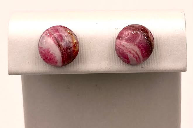 A pair of round stud earrings with pink, white, and red marbled stone patterns, displayed on a white rectangular jewelry stand against a white background.