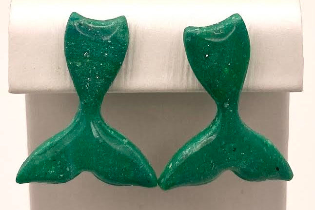A pair of green mermaid tail stud earrings displayed on a white jewelry stand against a white background.