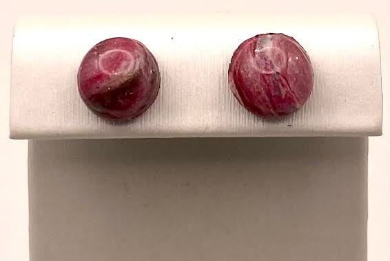 A pair of round, deep red gemstone stud earrings displayed on a white jewelry stand against a light background.