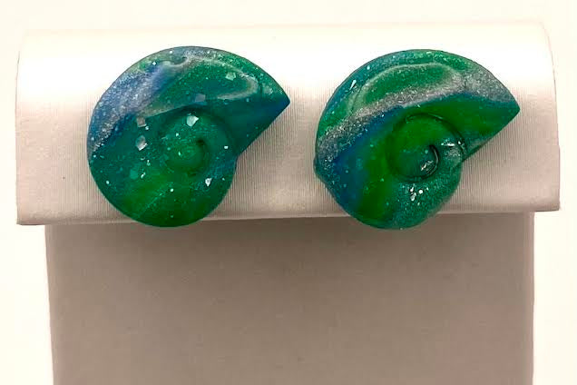 A pair of green and blue marbled spiral stud earrings displayed on a white jewelry stand against a white background.