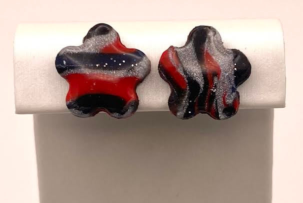A pair of marbled polymer clay earrings with swirls of black, red, and white, displayed on a white jewelry stand against a light background.