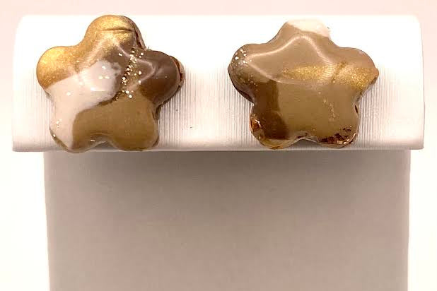 A pair of star-shaped stud earrings with a marbled pattern of gold, brown, and white, displayed on a white rectangular stand against a white background.