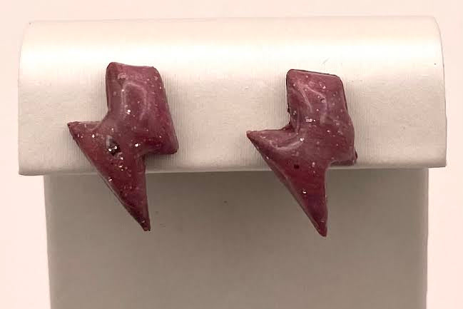 A pair of small lightning-bolt stud earrings in a dusty burgundy-red color with tiny silver flecks, displayed on a white jewelry stand.