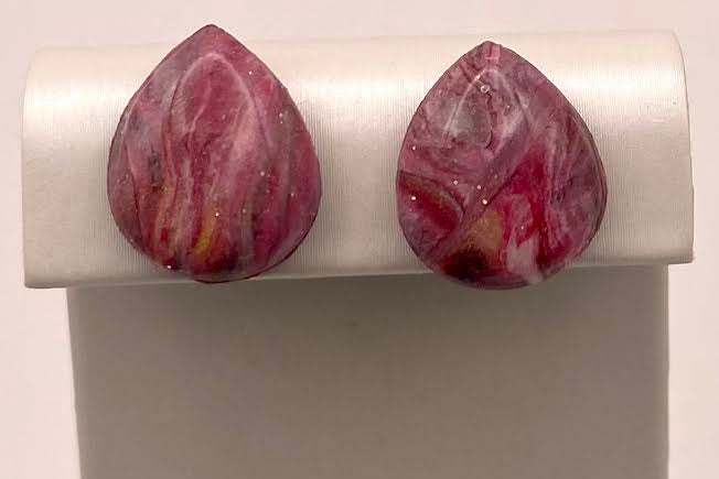 A pair of teardrop-shaped stud earrings with a marbled pink, white, and yellow stone pattern, displayed on a white jewelry stand.