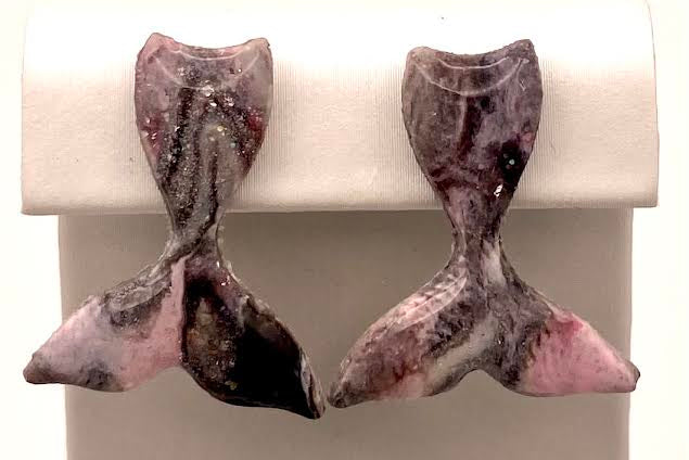 A pair of handmade mermaid tail earrings made from polished pink and black tourmaline, displayed on a white rectangular stand.