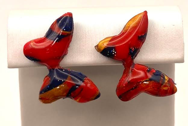 A pair of colorful, abstract butterfly-shaped earrings with red, blue, and orange marbled patterns, displayed on a white jewelry stand.