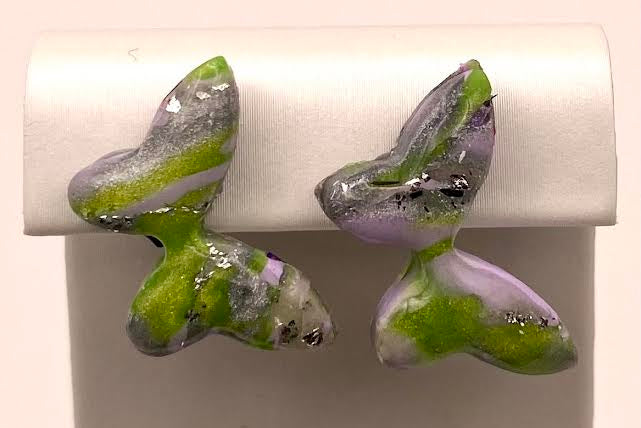 A pair of handmade polymer clay butterfly earrings in green, lavender purple, and silver, displayed on a white jewelry stand.