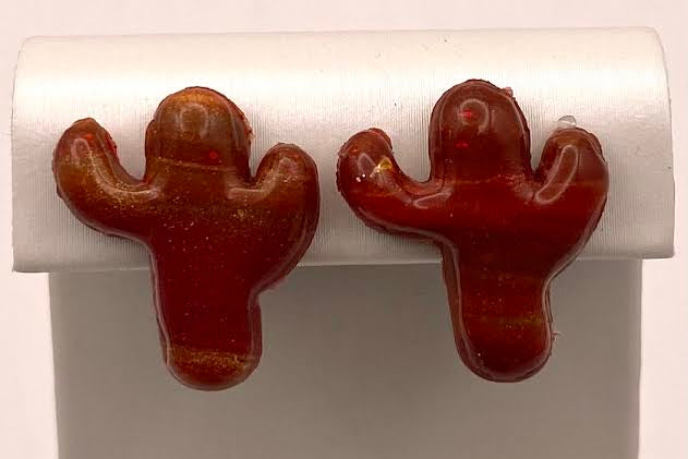 A pair of small cactus-shaped stud earrings in glossy reddish-brown resin, displayed on a white jewelry stand against a white background.
