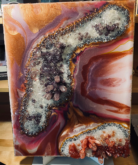 A square abstract painting depicting geode or agate-like formations with swirling copper, pink, purple, white, and brown marbled patterns, shown leaning against a stand in an indoor setting.