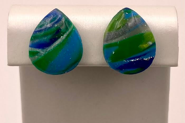 A pair of teardrop-shaped stud earrings with marbled blue, green, and white swirls, displayed on a white jewelry stand.