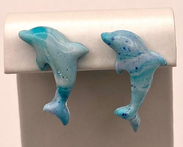 A pair of blue and white dolphin-shaped stud earrings displayed on a white jewelry stand against a light beige background.