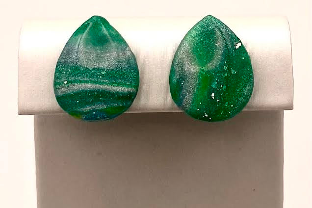 A pair of green teardrop-shaped stud earrings with a marbled pattern of dark and light green, displayed on a white jewelry stand against a light background.