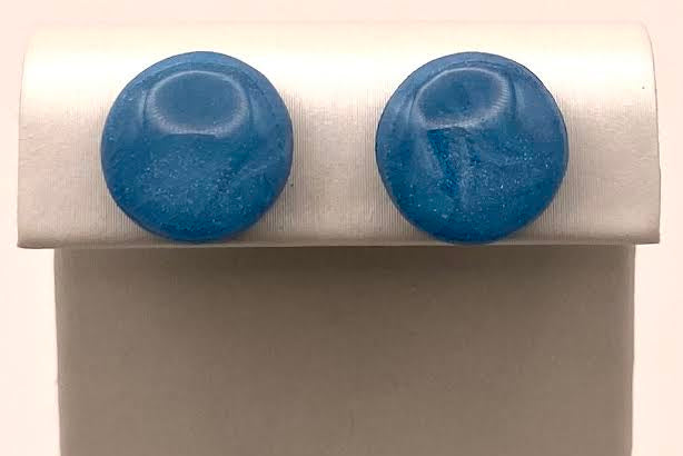 A pair of round blue stud earrings displayed on a white jewelry stand against a light background.