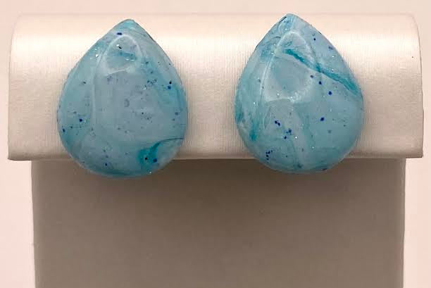 A pair of teardrop-shaped light blue marbled gemstone stud earrings displayed on a white jewelry stand against a light background.
