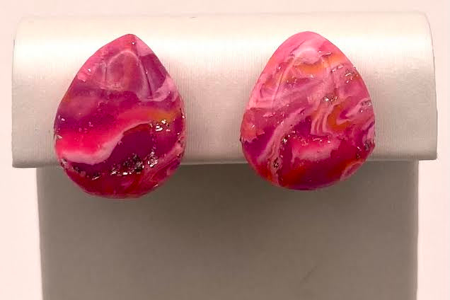 A pair of teardrop-shaped stud earrings with a vibrant pink and magenta marbled pattern, displayed on a white jewelry stand against a light background.