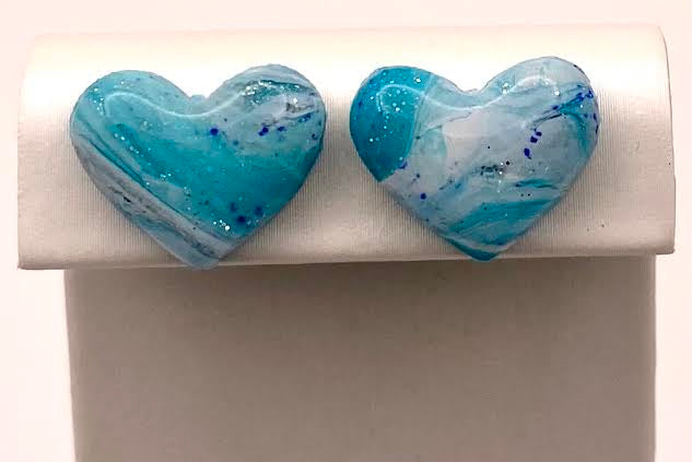 A pair of heart-shaped stud earrings with a blue and white marbled pattern, displayed on a white jewelry stand.