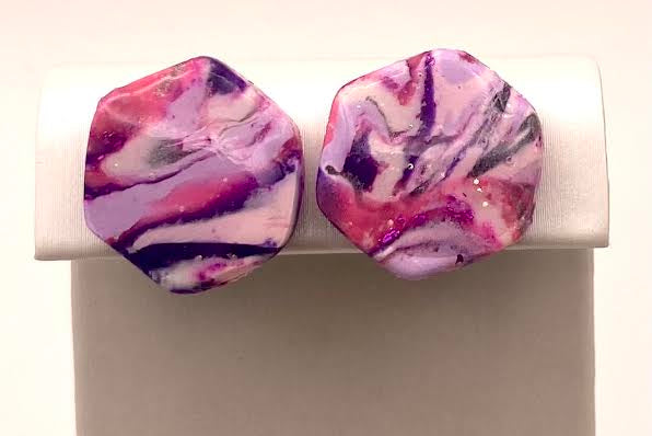 A pair of irregularly shaped stud earrings with a marbled pattern of pink, purple, and white, displayed on a white stand against a light gray background.