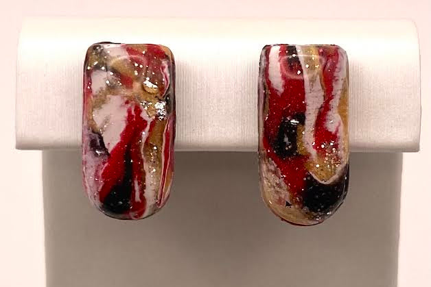 A pair of rectangular glass stud earrings with a marbled pattern of red, black, white, and gold, displayed on a white jewelry stand.