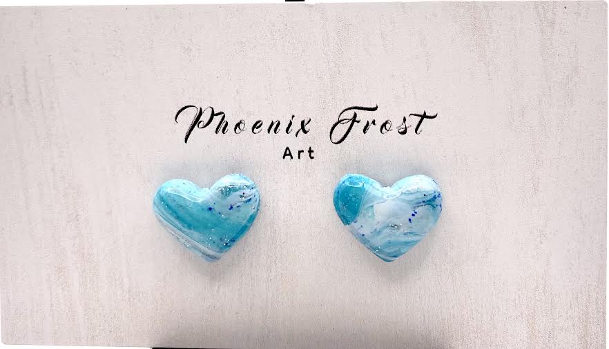 Two heart-shaped stud earrings with a blue and white marbled pattern, displayed on a light textured background with the text 'Phoenix Frost Art' above them.
