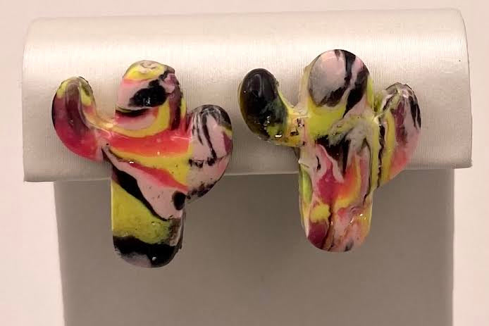 A pair of cactus-shaped stud earrings with a marbled pattern of pink, yellow, black, and white, displayed on a white jewelry stand.