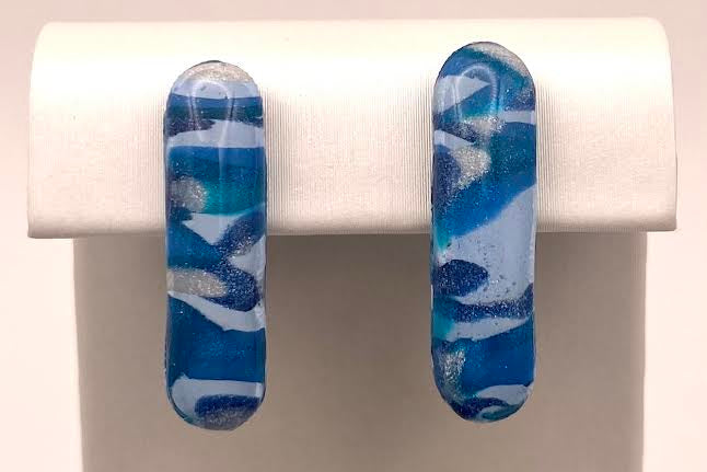 A pair of handmade rectangular stud earrings with a blue and white marbled pattern, displayed on a white jewelry stand against a light background.