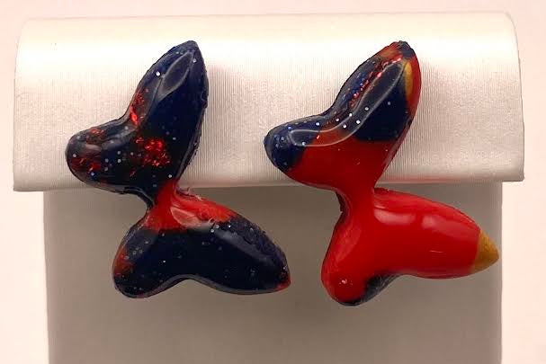 A pair of handmade, organic-shaped earrings in glossy black and red with tiny orange and yellow flecks, displayed on a white jewelry stand.