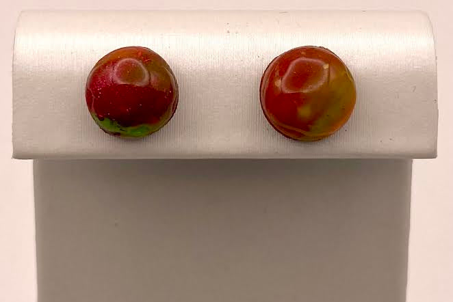 A pair of round marbled red and yellow cabochon stud earrings displayed on a white jewelry stand against a light background.