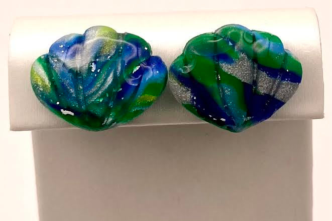 A pair of handmade glass stud earrings with a marbled swirl pattern of green, blue, and white, displayed on a white rectangular stand.